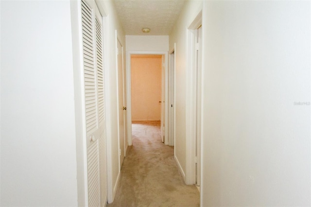 corridor featuring light colored carpet and a textured ceiling