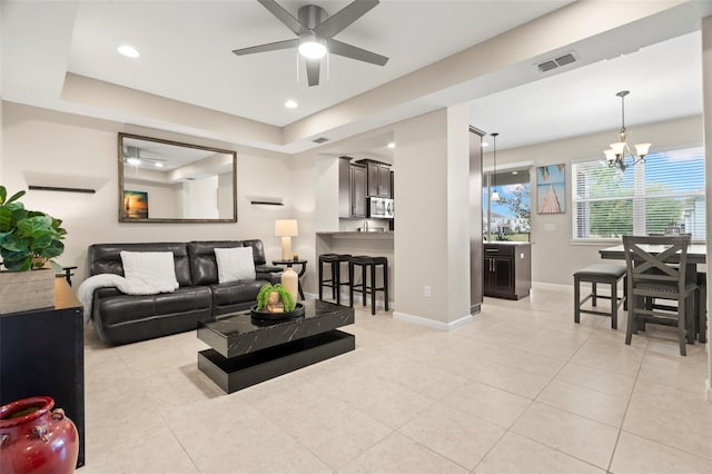 tiled living room featuring ceiling fan with notable chandelier and a tray ceiling