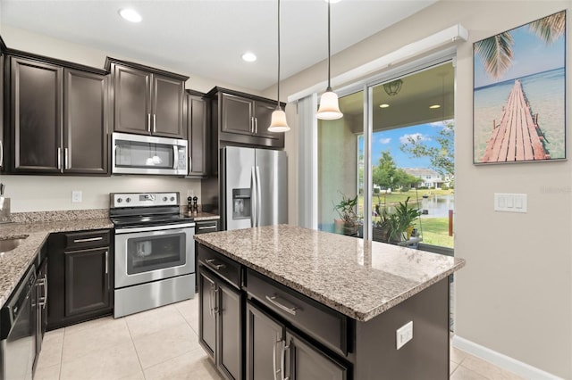 kitchen with light tile patterned floors, appliances with stainless steel finishes, a kitchen island, pendant lighting, and light stone countertops