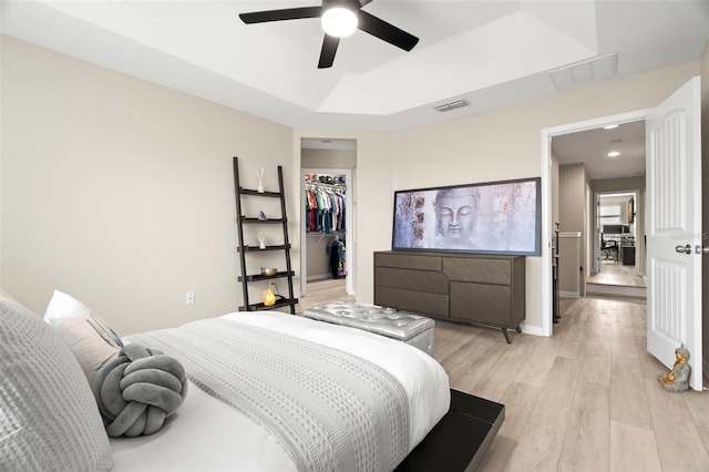 bedroom with a spacious closet, ceiling fan, a tray ceiling, light wood-type flooring, and a closet