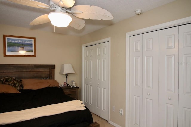 tiled bedroom featuring multiple closets, a textured ceiling, and ceiling fan