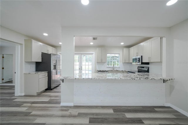 kitchen featuring light hardwood / wood-style floors, light stone countertops, stainless steel appliances, kitchen peninsula, and white cabinets