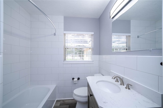 full bathroom with vanity, tile walls, tiled shower / bath combo, toilet, and a textured ceiling