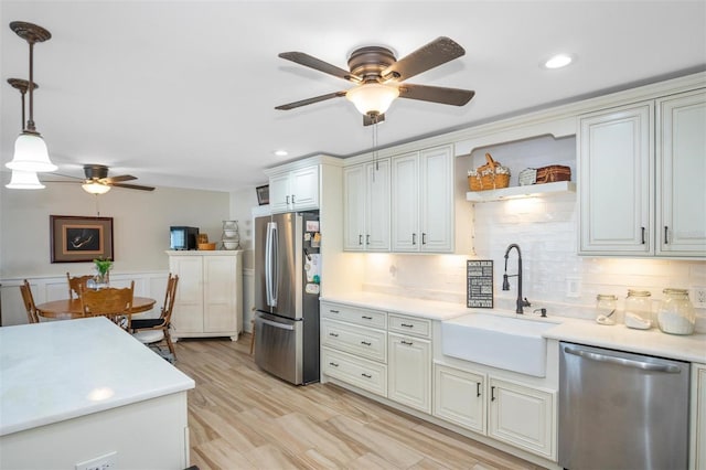 kitchen with sink, stainless steel appliances, tasteful backsplash, decorative light fixtures, and light wood-type flooring