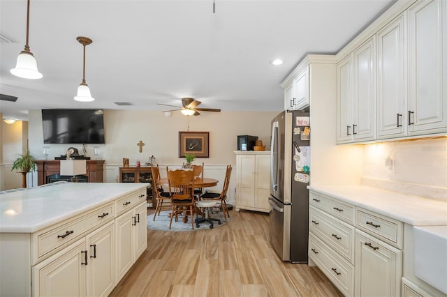 kitchen featuring light hardwood / wood-style flooring, decorative backsplash, stainless steel fridge, ceiling fan, and decorative light fixtures