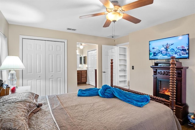 bedroom with a ceiling fan, a glass covered fireplace, visible vents, and ensuite bath