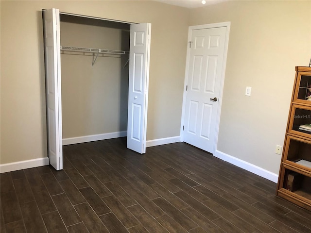 unfurnished bedroom featuring dark wood-style flooring, a closet, and baseboards