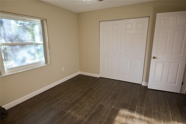 unfurnished bedroom with dark wood-style floors, a closet, and baseboards