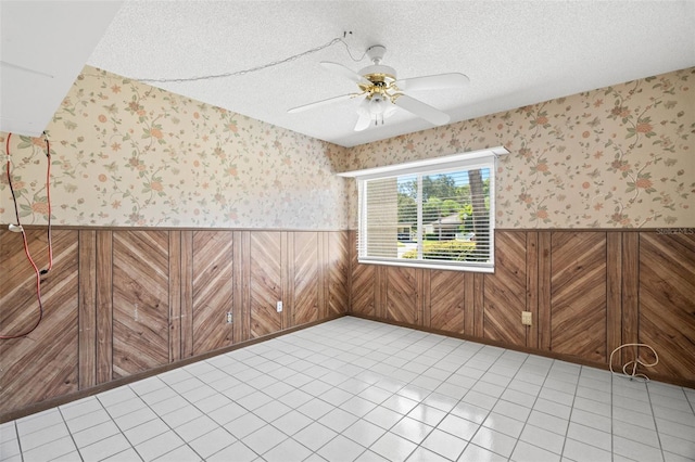 tiled spare room featuring wood walls, a textured ceiling, and ceiling fan