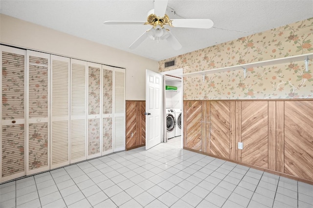 unfurnished bedroom with a closet, independent washer and dryer, wood walls, and ceiling fan