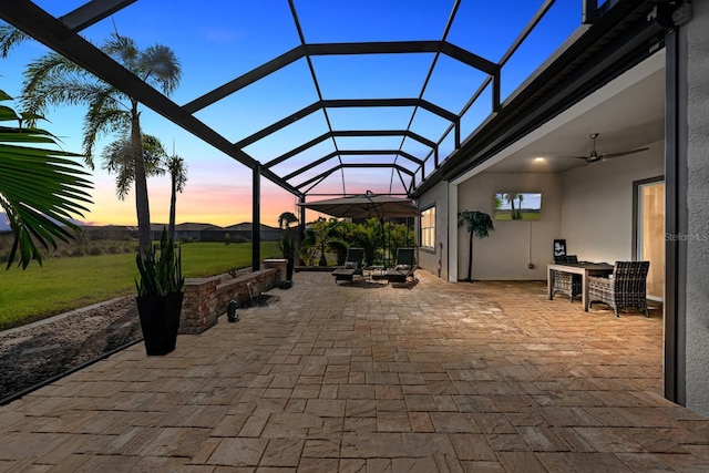 patio terrace at dusk featuring glass enclosure and ceiling fan