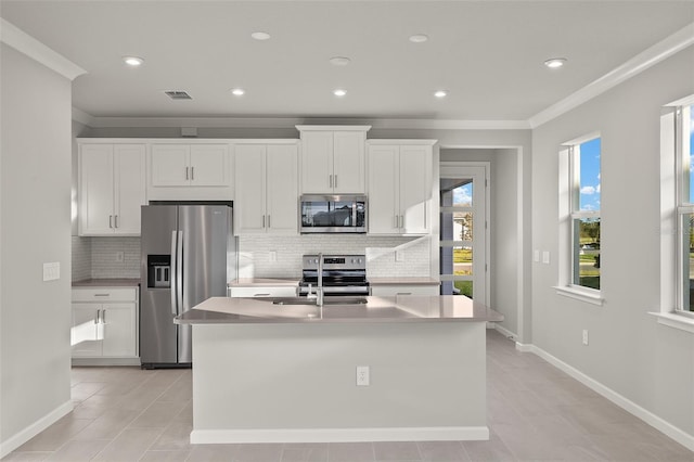 kitchen with decorative backsplash, white cabinets, an island with sink, and appliances with stainless steel finishes