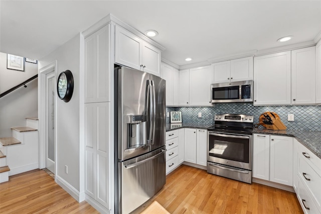 kitchen featuring tasteful backsplash, light wood-type flooring, dark stone counters, stainless steel appliances, and white cabinets