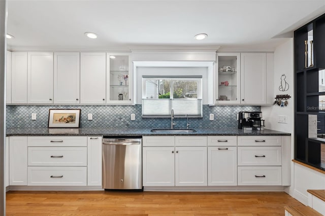 kitchen featuring stainless steel dishwasher, dark stone counters, sink, and white cabinets