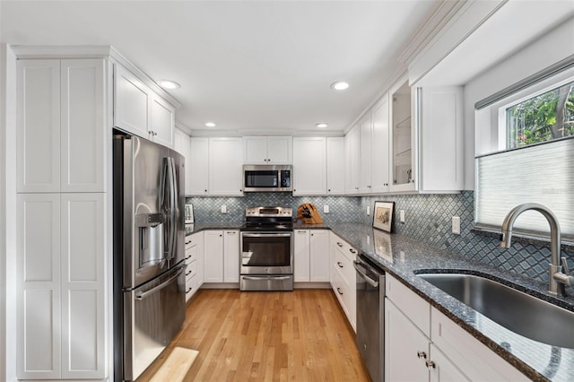 kitchen featuring sink, dark stone countertops, light wood-type flooring, stainless steel appliances, and white cabinets