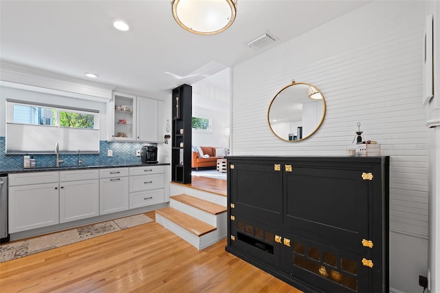 kitchen with tasteful backsplash, white cabinetry, sink, dark stone counters, and light hardwood / wood-style flooring