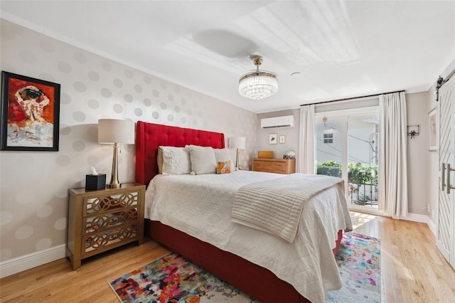 bedroom with a chandelier, access to outside, a wall unit AC, and light hardwood / wood-style flooring