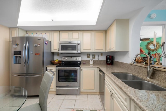 kitchen featuring cream cabinets, stainless steel appliances, sink, light tile patterned flooring, and light stone counters