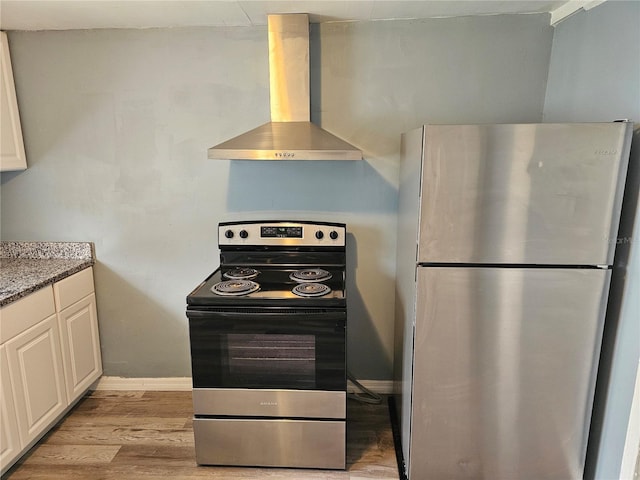 kitchen with wall chimney range hood, white cabinetry, stainless steel appliances, and light hardwood / wood-style floors