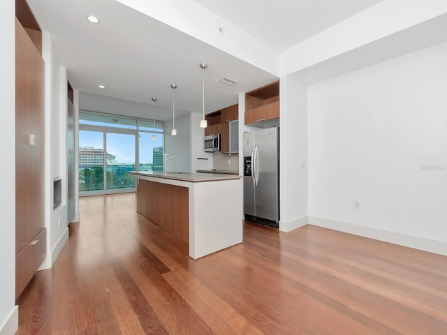 kitchen featuring appliances with stainless steel finishes, light hardwood / wood-style floors, a kitchen island with sink, and pendant lighting