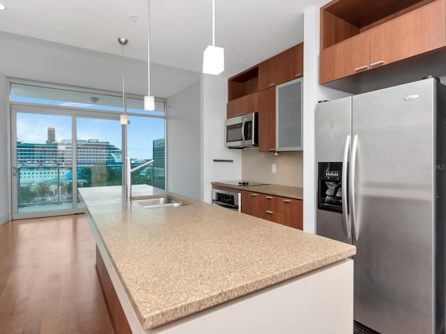 kitchen featuring sink, light hardwood / wood-style floors, decorative light fixtures, a center island with sink, and appliances with stainless steel finishes