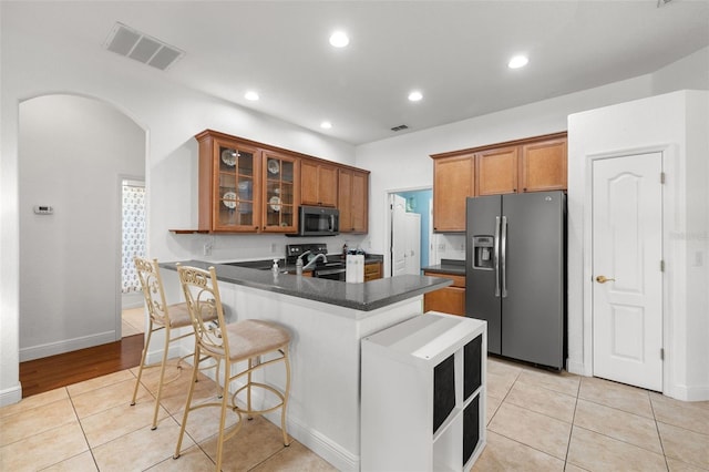 kitchen featuring appliances with stainless steel finishes, kitchen peninsula, light tile patterned flooring, and a kitchen breakfast bar