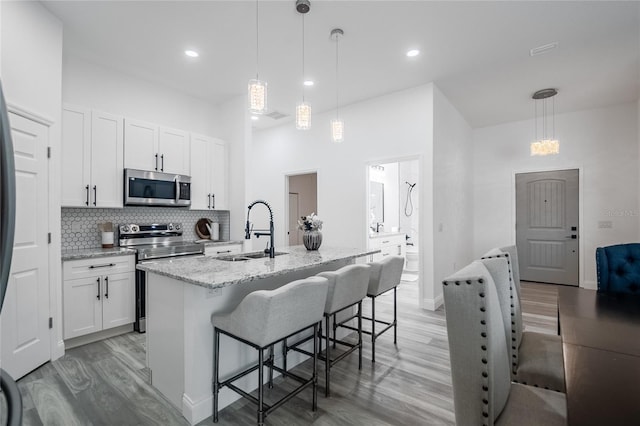 kitchen with a center island with sink, white cabinets, sink, appliances with stainless steel finishes, and decorative light fixtures