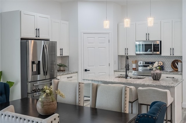 kitchen featuring backsplash, a kitchen island with sink, white cabinets, and appliances with stainless steel finishes