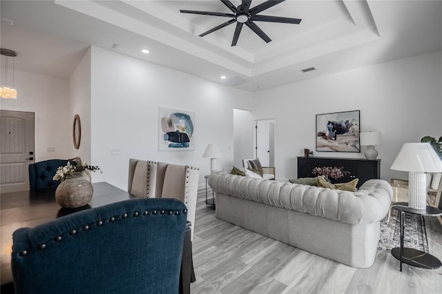 living room with ceiling fan, a raised ceiling, and light wood-type flooring