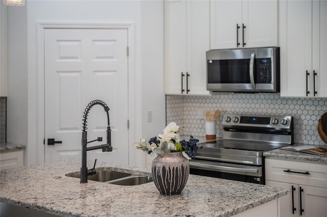 kitchen with stainless steel appliances, white cabinets, a kitchen island with sink, and a sink