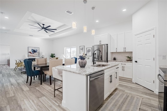 kitchen featuring appliances with stainless steel finishes, a raised ceiling, white cabinets, and an island with sink