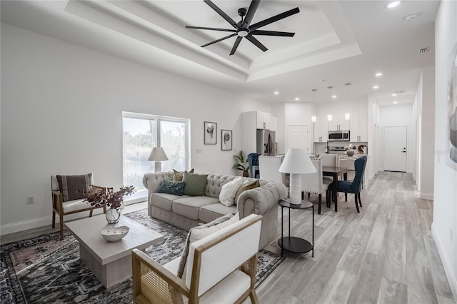 living room with baseboards, recessed lighting, a raised ceiling, and light wood-style floors