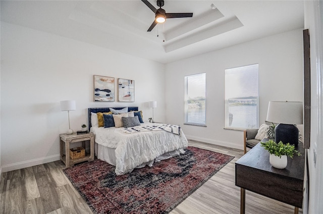 bedroom featuring a raised ceiling, baseboards, and wood finished floors