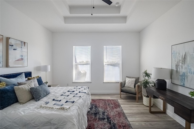 bedroom with a ceiling fan, a raised ceiling, baseboards, and wood finished floors