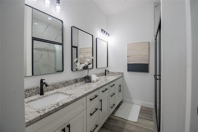 full bathroom with double vanity, a marble finish shower, baseboards, and a sink