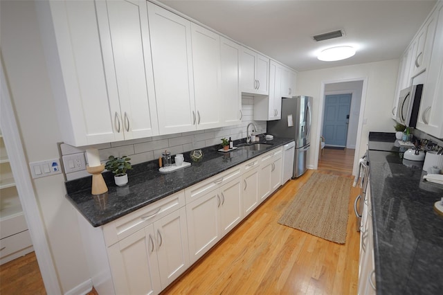 kitchen with white cabinets, decorative backsplash, light hardwood / wood-style floors, and dark stone counters