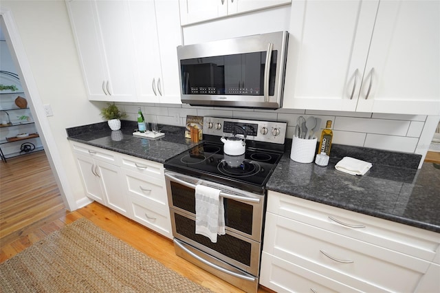 kitchen with decorative backsplash, white cabinets, light hardwood / wood-style floors, and appliances with stainless steel finishes