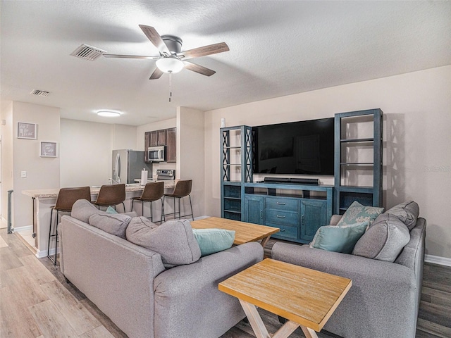 living room featuring a textured ceiling, light wood-type flooring, and ceiling fan