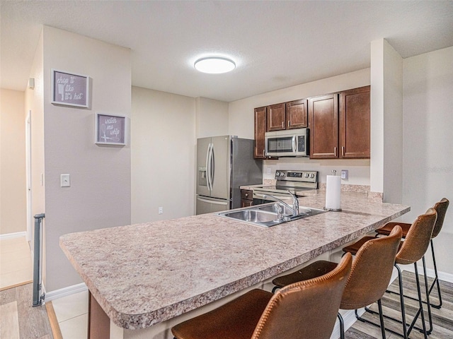 kitchen with a breakfast bar area, appliances with stainless steel finishes, kitchen peninsula, and light hardwood / wood-style floors