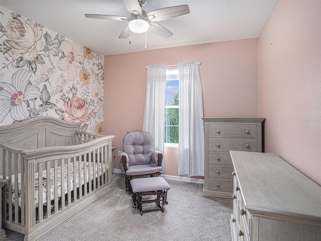 bedroom with a nursery area, light colored carpet, and ceiling fan