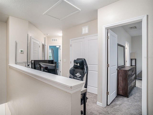 hall with a textured ceiling and light colored carpet