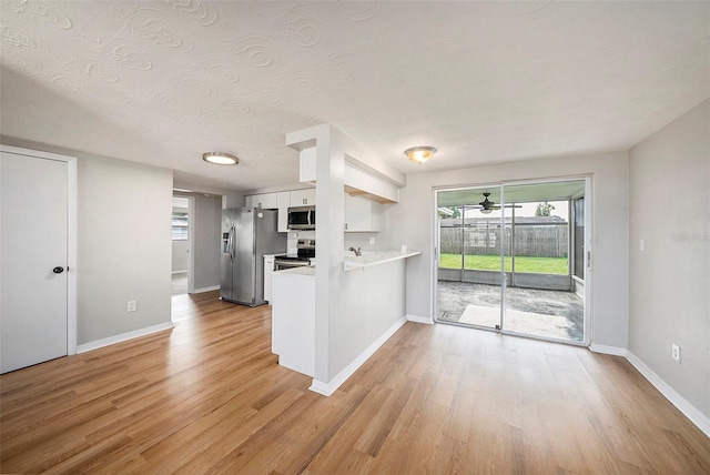 kitchen featuring light hardwood / wood-style flooring, kitchen peninsula, stainless steel appliances, white cabinets, and a textured ceiling