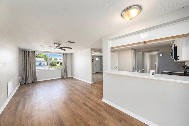 unfurnished living room featuring a textured ceiling, wood-type flooring, and ceiling fan