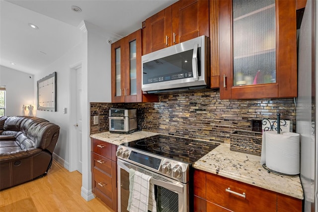 kitchen featuring decorative backsplash, light stone countertops, stainless steel appliances, and light wood-type flooring