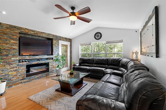 living room featuring hardwood / wood-style floors, vaulted ceiling, a stone fireplace, and ceiling fan