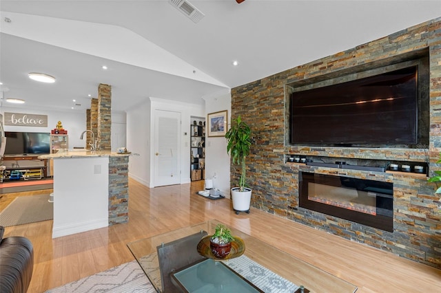 living room featuring sink, lofted ceiling, light wood-type flooring, and a fireplace