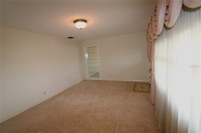 spare room featuring light carpet, a healthy amount of sunlight, and visible vents