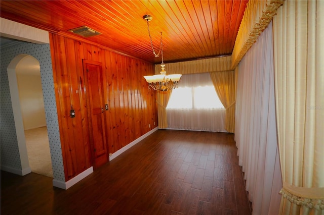 unfurnished dining area featuring dark wood-type flooring, wood ceiling, an inviting chandelier, and wood walls