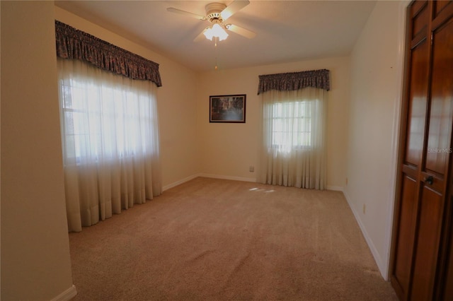 spare room featuring light carpet, baseboards, and ceiling fan