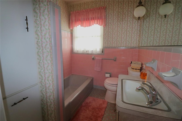 bathroom with wallpapered walls, toilet, a sink, and wainscoting